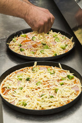 Two black metal baking sheets with raw pizza.