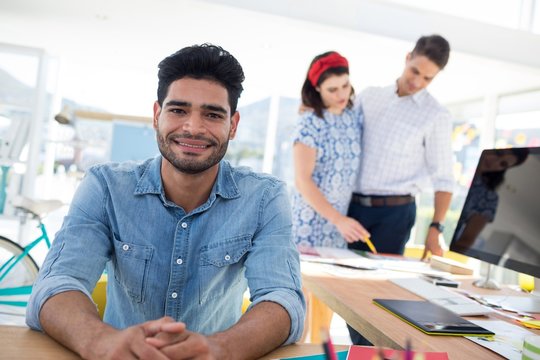 Male graphic designer relaxing while coworkers working in the office