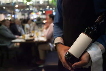 Blurry background waiter holding wine on hand ready to serving to customer in restaurant.