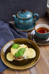 Breakfast. Juicy Egg Benedict Brunch. Hot black tea. Cup. Teapot. Wooden table.