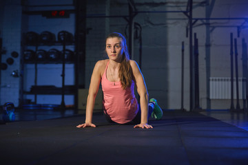 Fototapeta premium Fit woman in colourful sportswear doing burpees on a exercise mat in a grungy industrial type space