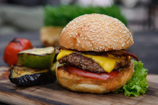 Cheeseburger on the wooden table with grilled vegetables