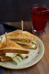 Club sandwich with cheese, ham, lettuce and cucumber on plate and glass of cranberry juice