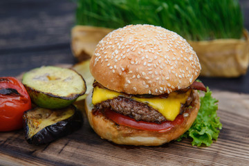 Cheeseburger on the wooden table outdoors. served with grilled vegetables. Home made fast food from fresh, tasty ingredients. Hamburger with crispy beckon and tomato inside