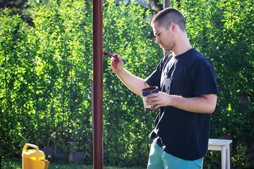 Young man with paintbrush painting pipe in his yard