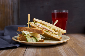 Club sandwich with cheese, ham, lettuce and cucumber with toasted bread on plate and glass of cranberry juice