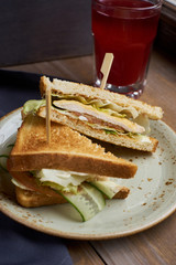 Club sandwich with cheese, ham, lettuce and cucumber with toasted bread on plate and glass of cranberry juice