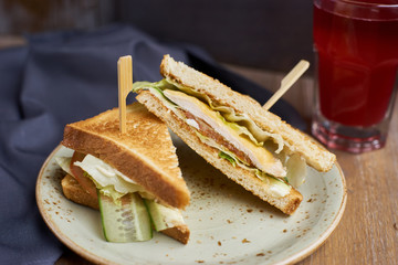 Two Club sandwich with cheese, ham, lettuce and cucumber on plate and glass of cranberry juice on wooden table