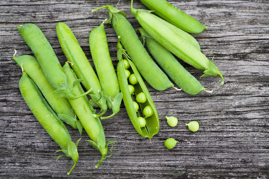 Pods of green peas on a old wooden surface close up, top view