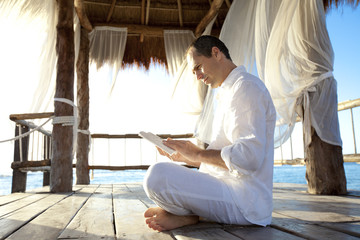 homme qui lit assis sur une terrasse au bord de la mer