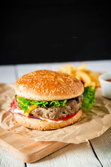 American tasty hamburger with tasty beef, sauce and french fries on dark background.