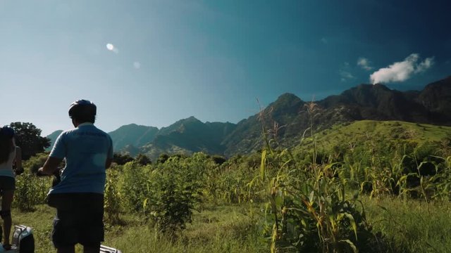 Three people on segway in Pemuteran hills in front of mountains, balinese men and caucasian woman, view from the back
