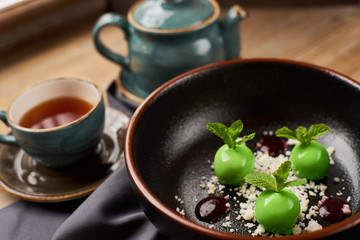 Small green apples desert with chocolate, mint leafs and caramel served in big black plate. Hot black tea.