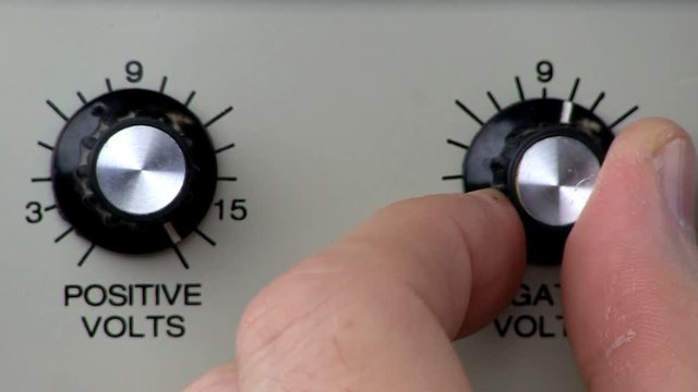 A man turns knob counter clockwise to decrease negative voltage from power supply