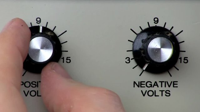 A man turns knob counter clockwise to decrease positive voltage from power supply