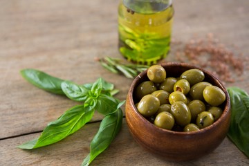 Marinated green olives in bowl and oil container with green leaf on table