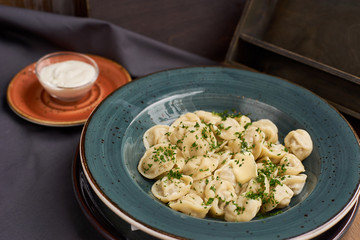 Meat dumplings - russian pelmeni, ravioli with meat on a blue ceramic plate and sour cream on a wooden table
