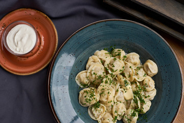 Meat dumplings - russian pelmeni, ravioli with meat on a blue ceramic plate and sour cream on a wooden table