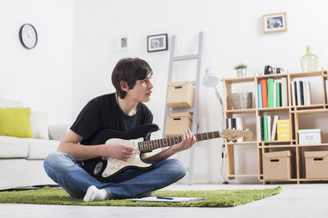 Young boy teenager in a children's room writes and composes a song on a guitar