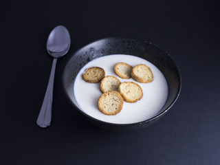 Danish koldskaal - cold buttermilk soup with crispy biscuits named kammerjunker served in rustic black bowl, isolated on black background
