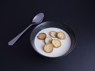 Danish koldskaal - cold buttermilk soup with crispy biscuits named kammerjunker served in rustic black bowl, isolated on black background