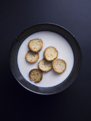 Danish koldskaal - cold buttermilk soup with crispy biscuits named kammerjunker served in rustic black bowl, isolated on black background