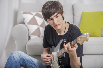 Young boy teenager in a children's room writes and composes a song on a guitar