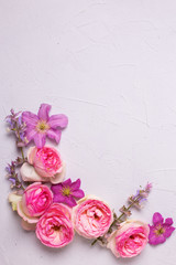 Pink roses and violet summer clematis flowers on grey textured background.
