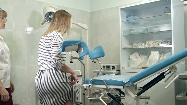 Gynecologist asking female patient to sit on gynecological chair for examination