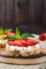 A small bruschetta with curd and fresh strawberries on a dark wooden background. Proper nutrition. Vertical view.