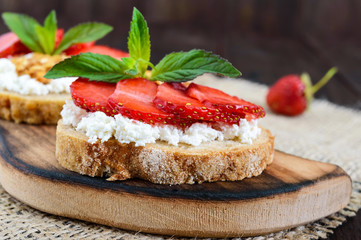 A small bruschetta with curd and fresh strawberries on a dark wooden background. Proper nutrition.