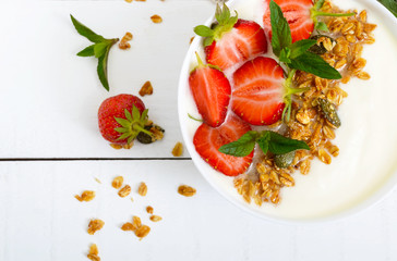 A bowl of dietary fitness breakfast: yogurt, granola, fresh strawberry, mint on a white wooden background. Proper nutrition. Top view.