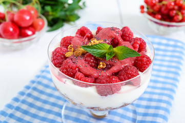 Sweet creamy dessert with granola, cream cheese, fresh raspberries in a glass bowl on a white wooden background. Close up