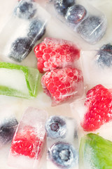 Summer berries. Raspberries, blueberries and mint leaves in ice cubes on a white background. Vertical format