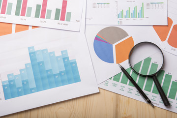 Magnifying glass and documents with analytics data lying on wood table