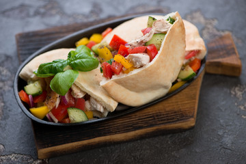 Pitas with roasted chicken meat and fresh vegetables served in a metal plate on a wooden chopping board, studio shot