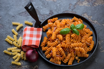 Frying pan with fusilli wheat pasta over brown stone background, horizontal shot