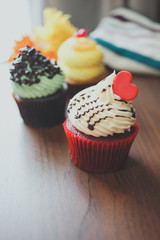 Three cupcakes of yellow, red, and green are arranged on table.