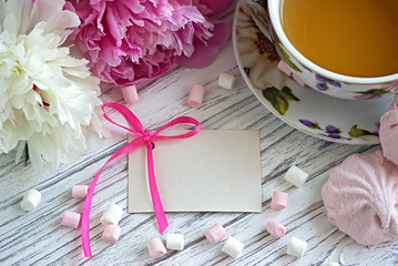 Peonies flowers pink cup of tea greeting card marshmallow on a white wooden background - stock image.