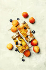 Icy refreshing drink with apricots, blueberries and ice in the bottles, food background, top view