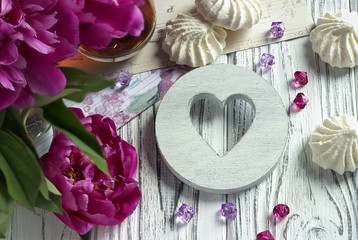 Peonies flowers pink glass of tea with white wooden heart marshmallow on a white wooden background - stock image.