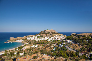 Fototapeta na wymiar Lindos town at the foot of the mountain. Acropolis of Lindos is located on a hill above the town. Bay and harbor with beach.