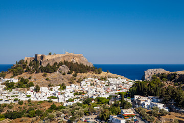 Obraz premium Lindos town at the foot of the mountain. Acropolis of Lindos is located on a hill above the town. Bay and harbor with beach.