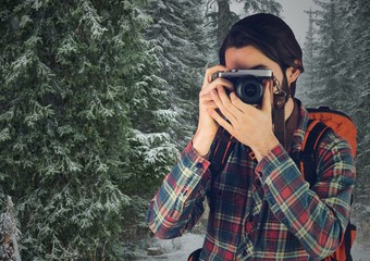 Millennial backpacker with camera against snowy trees