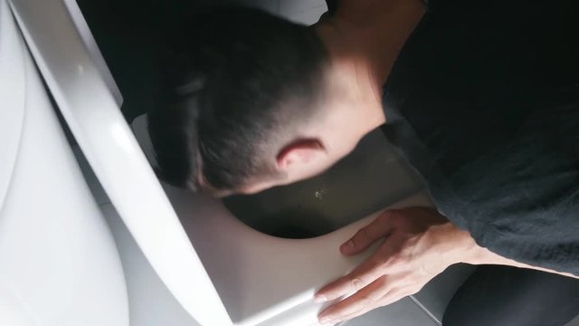 A man throwing up violently into the toilet in the bathroom