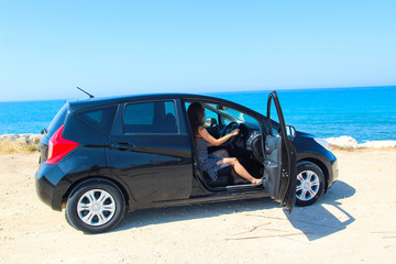 A woman sitting inside a rented car with a sea view