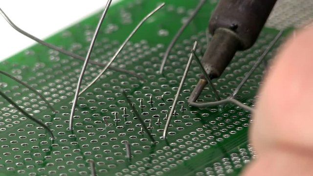 An electrical engineer builds a circuit design by soldering a through hole IC to a breadboard by hand