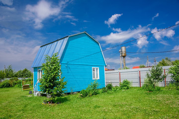 Fototapeta na wymiar Bright blue summer house, fence and electrical wires on a background of blue sky with white clouds at summer sunny day in countryside