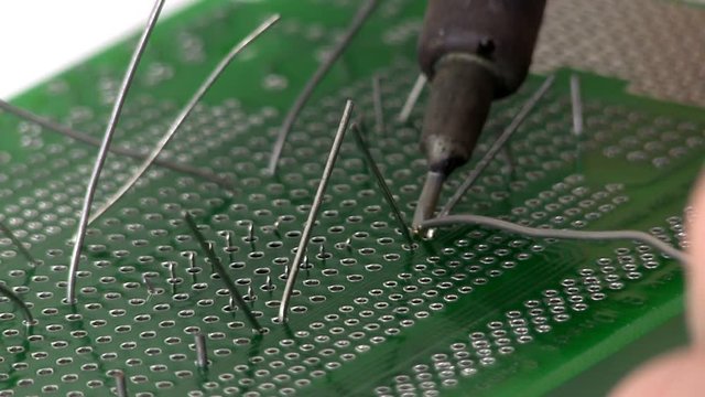 An electrical engineer builds a circuit design by soldering through hole components to a breadboard by hand