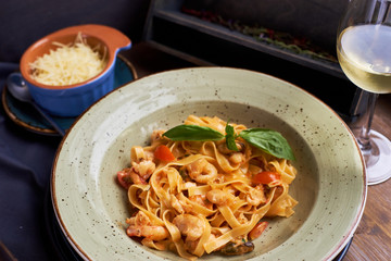 Seafood pasta. Tagliatelle with prawns and spices in tomato-cream sauce. Glass of white wine.